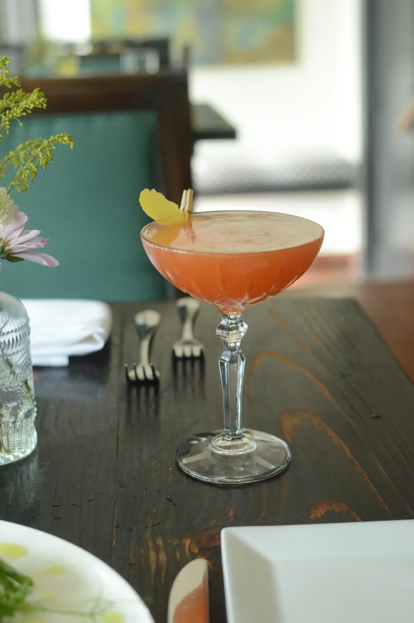 A pink cocktail in a coupe glass on a dark wood table.